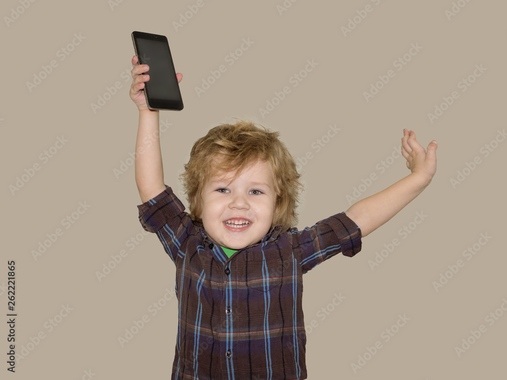 A little toddler boy picks up a smartphone gadget above his head. A satisfied child is happy that he was allowed to play phones with his smartphone. A little toddler boy picks up a smartphone gadget above his head. A satisfied child is happy that he was allowed to play phones with his smartphone.