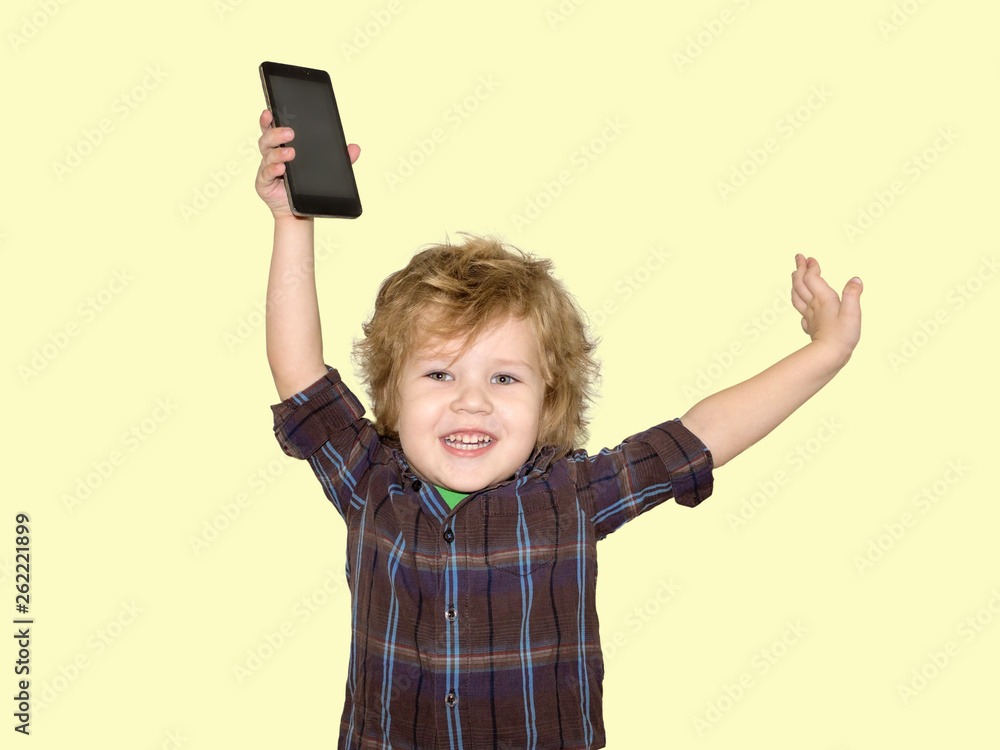 A little toddler boy picks up a smartphone gadget above his head. A satisfied child is happy that he was allowed to play phones with his smartphone. A little toddler boy picks up a smartphone gadget above his head. A satisfied child is happy that he was allowed to play phones with his smartphone.