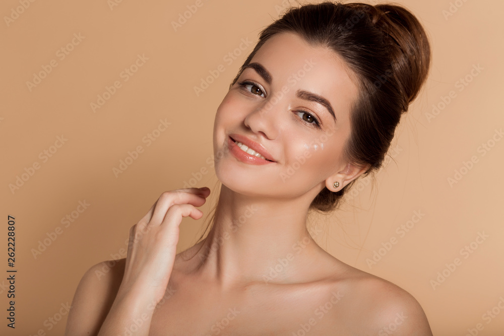 Beautiful face portrait of young woman is applying face cream on a cheek. Skin care and health concept. Beautiful face portrait of young woman is applying face cream on a cheek. Skin care and health concept.