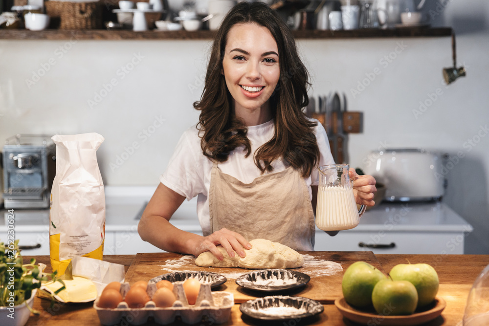 Cheerful young woman wearing apron preparing dough