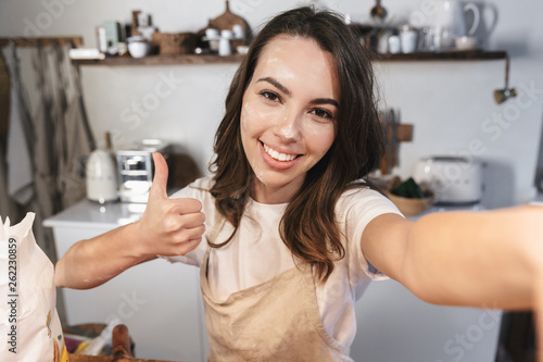 Cheerful young girl covered with flour taking a selfie