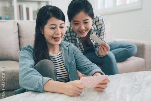 Happy asian friends looking at smartphone screen watching funny video relax at home. beautiful women friends using cellphone having fun laughing in living room playing online game on internet