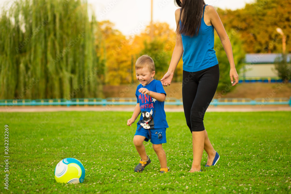 DNEPR, UKRAINE - AUGUST 13, 2018: Mother and little son playing ball on grass in summer park.