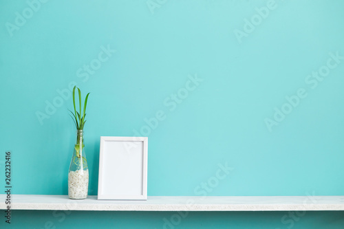 Modern room decoration with Picture frame mockup. White shelf against pastel turquoise wall with spider plant cuttings in water.