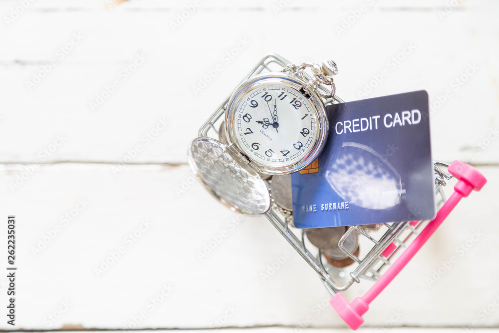 Beautiful silver watch necklace and coin with credit cards on mini shopping cart on white wooden floor Beautiful silver watch necklace and coin with credit cards on mini shopping cart on white wooden floor