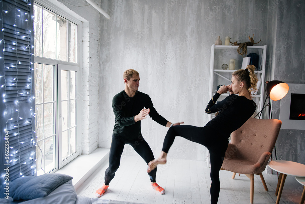 Obraz premium The guy and the girl in tracksuit. Black sports uniform. Male and female athletes. Pumped up body. Triathlon. Morning work-out. Set of exercises for body. Classes in pair. Workout together at home.
