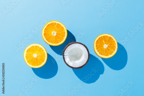 Cut oranges and coconuts on a blue background. Hard light. Tropics concept  healthy food  breakfast  diet  vacation. Flat lay  top view.