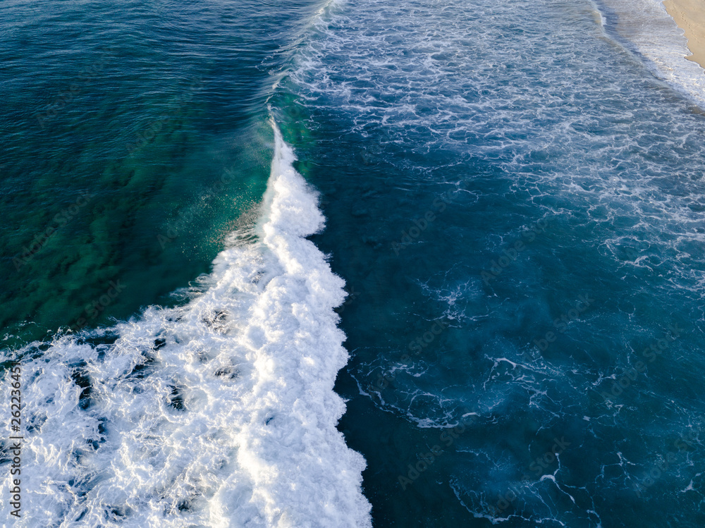 Aerial view of wave breaking into white foam on the coastline.