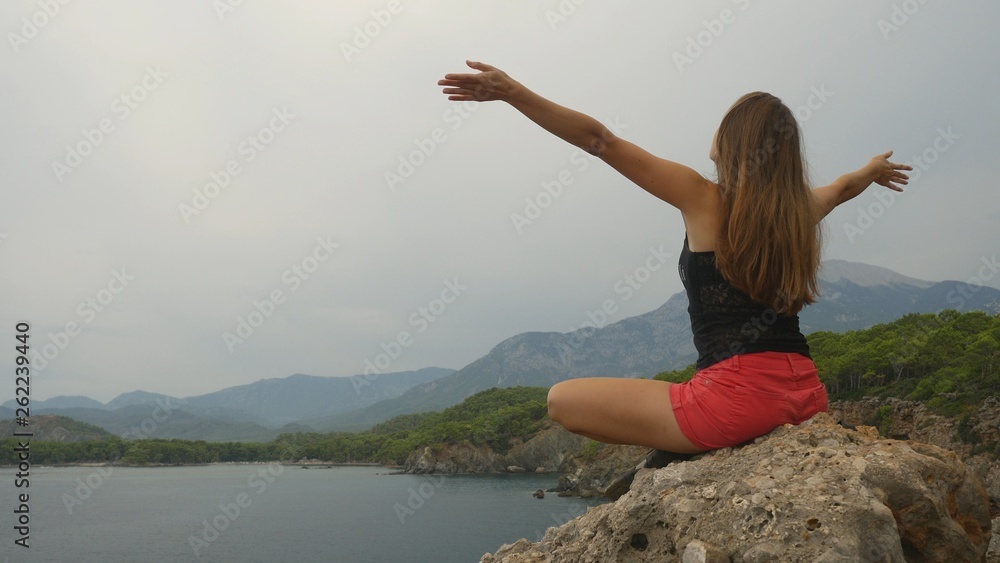 Female tourist sitting on a rock on clear sky and calm sea background Female tourist sitting on a rock on clear sky and calm sea background