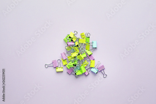 Top view of many multicolor binders clips on pastel purple background.Trendy neon colors. Group of paper clip different colors.