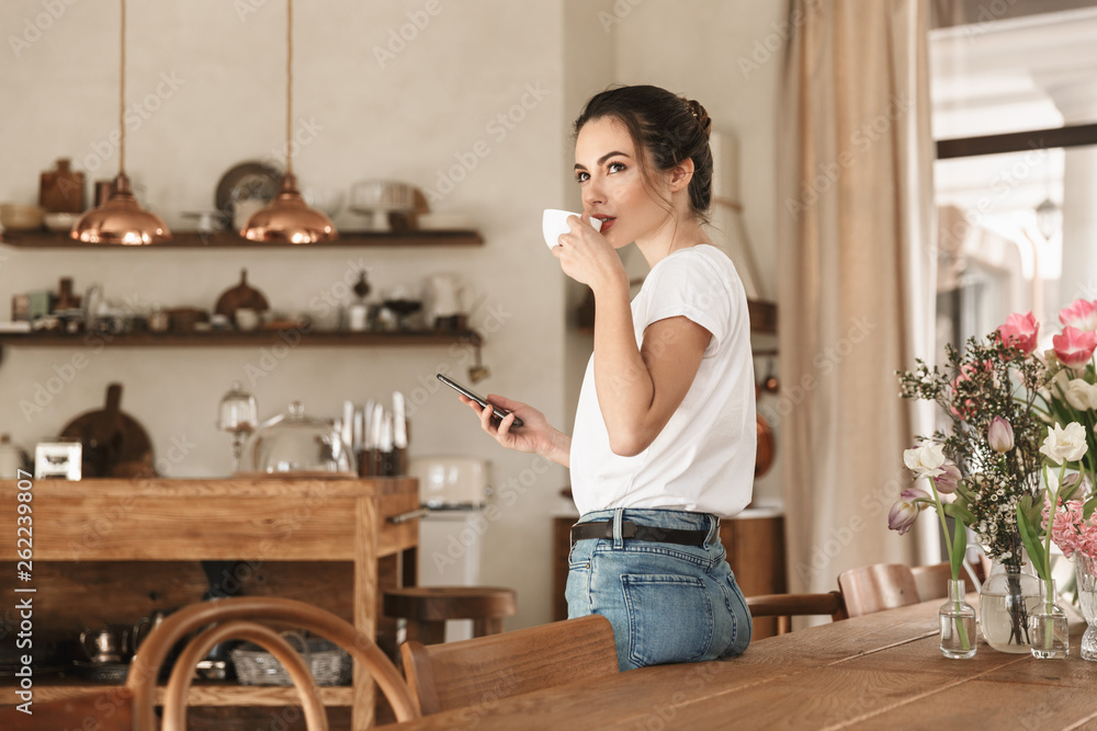 Beautiful young student girl drinking coffee posing indoors chatting by mobile phone. Beautiful young student girl drinking coffee posing indoors chatting by mobile phone.