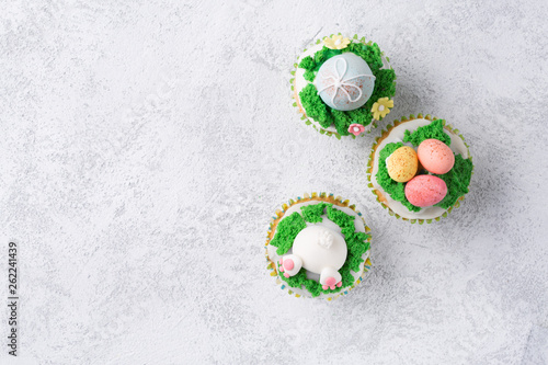 Festive cupcakes with funny bunny, eggs and grass on white background. Easter holiday concept. Top view with copy space