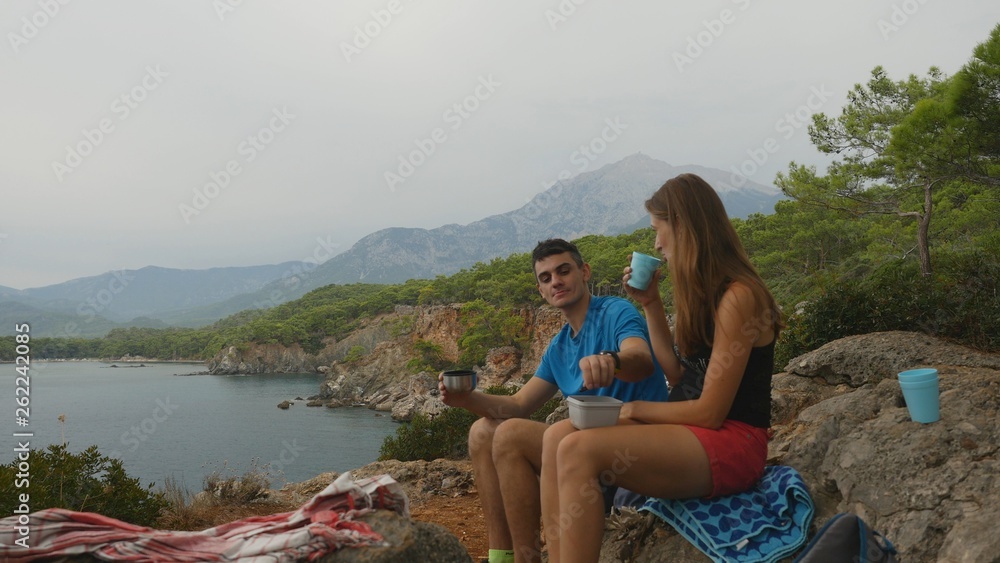 Young couple sitting on rocks in forest eating picnic