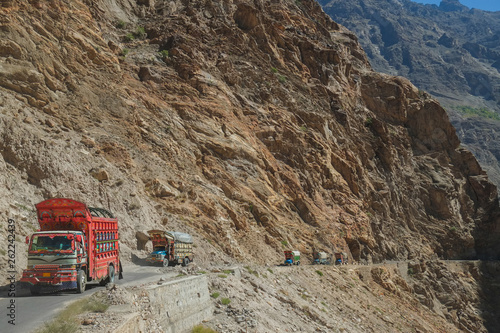 Pakistani decorated trucks travelling on dangerous paved road along the mountain near the cliff, transport goods via Karakoram highway. Gilgit Baltistan, Pakistan. photo