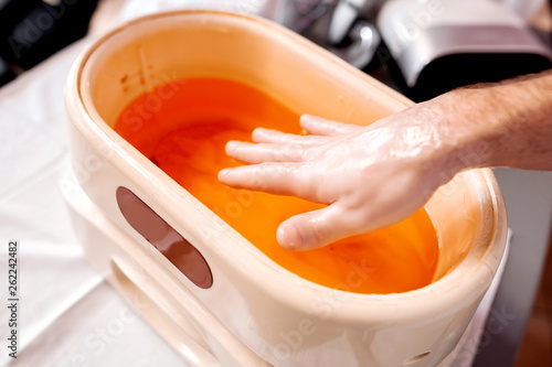 Close up of a male hand taken out from a paraffin bath during manicure treatment photo