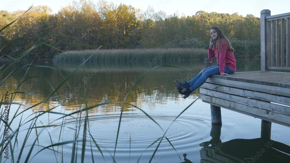 Young woman in pink pullower sitting on wooden dock over the water Young woman in pink pullower sitting on wooden dock over the water