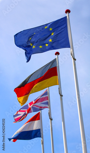 Flags from England, United Kingdom, Germany and Nederlands waving from flagpoles together with the EU, European Union, flag against a blue sky.