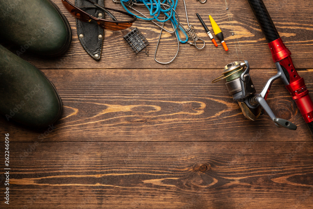 Fishing theme. Frame with rubber boots, rod with reel, fishing buoy, knife and fish string on wooden background. Free space Fishing theme. Frame with rubber boots, rod with reel, fishing buoy, knife and fish string on wooden background. Free space