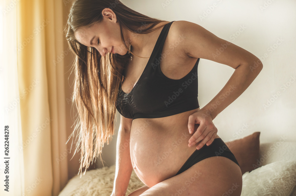 Pregnant woman in bra and panties holding stomach stock photo
