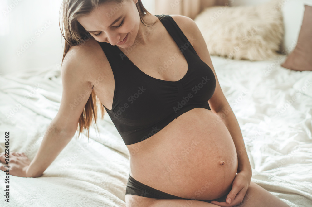 Attractive pregnant woman is sitting in bed and holding her belly. Last months of pregnancy Attractive pregnant woman is sitting in bed and holding her belly. Last months of pregnancy