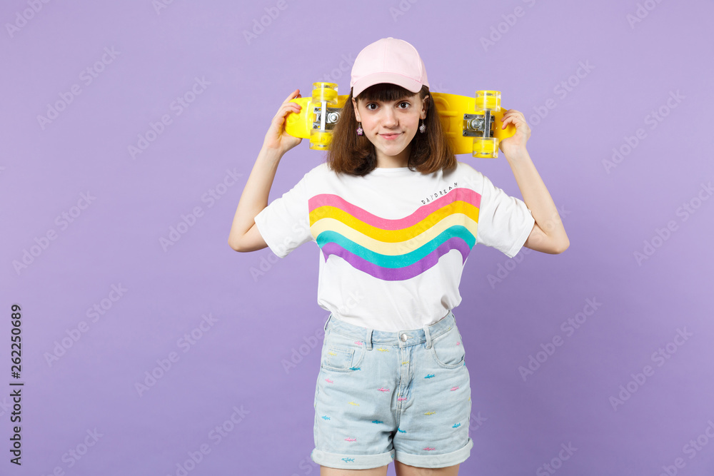 Portrait of smiling beautiful teen girl in vivid clothes holding yellow skateboard isolated on violet pastel wall background in studio. People sincere emotions, lifestyle concept. Mock up copy space. Portrait of smiling beautiful teen girl in vivid clothes holding yellow skateboard isolated on violet pastel wall background in studio. People sincere emotions, lifestyle concept. Mock up copy space.