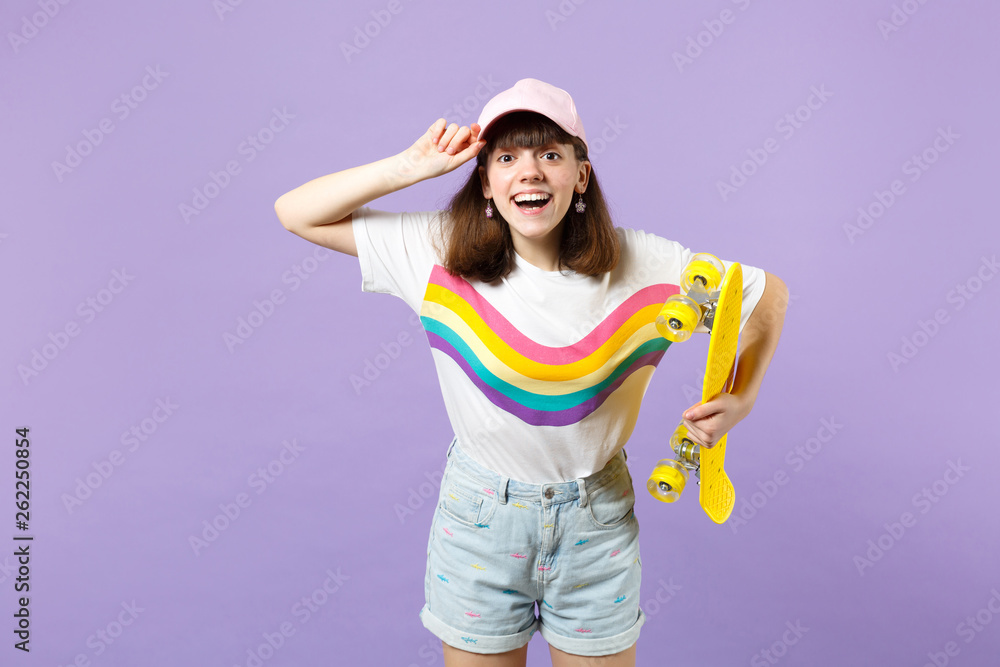 Portrait of funny teen girl in vivid clothes looking camera, holding yellow skateboard isolated on violet pastel background in studio. People sincere emotions, lifestyle concept. Mock up copy space. Portrait of funny teen girl in vivid clothes looking camera, holding yellow skateboard isolated on violet pastel background in studio. People sincere emotions, lifestyle concept. Mock up copy space.