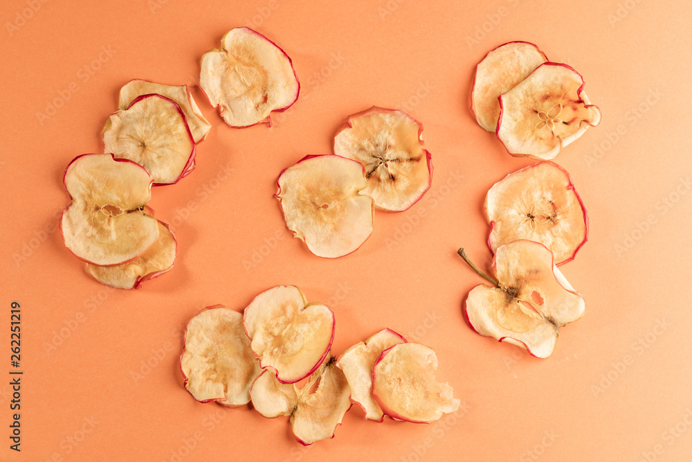 Healthy homemade pple chips are lying on coral background.