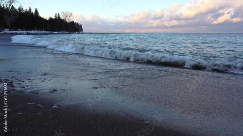 Icy blue water crashing onto a frozen beach at sunset. photo