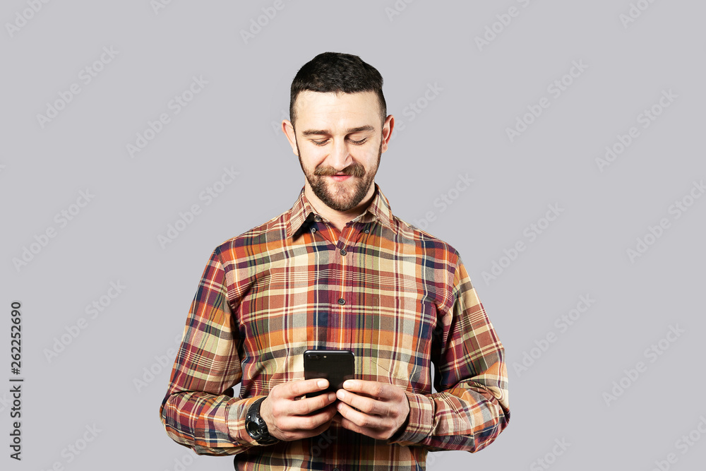 Young handsome man with facial hair posing over gray wall with a lot of copy space for text. Portrait of confident bearded male, wearing hipster slim fit checkered shirt. Isolated, background. Young handsome man with facial hair posing over gray wall with a lot of copy space for text. Portrait of confident bearded male, wearing hipster slim fit checkered shirt. Isolated, background.