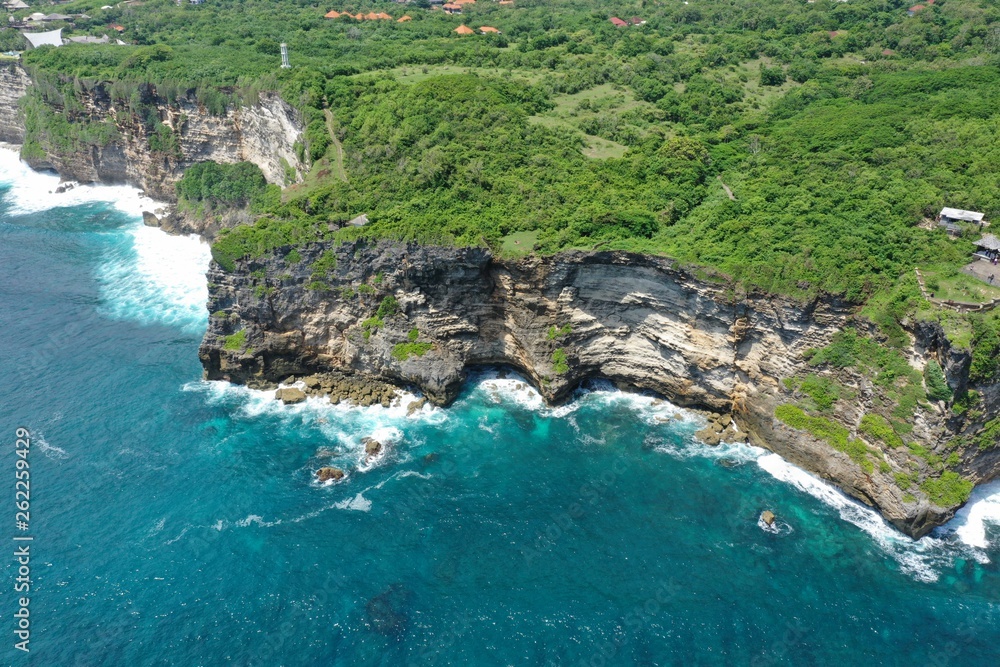 Aerial view of green cliff and blue ocean with breaking waves in Uluwatu Temple, Bali, Indonesia. Aerial view of green cliff and blue ocean with breaking waves in Uluwatu Temple, Bali, Indonesia.