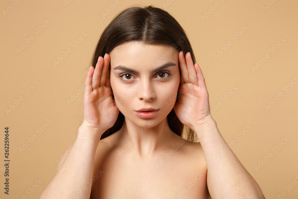 Fototapeta premium Bliska brunetka pół naga kobieta 20s z idealną skórą, nagi makijaż na białym tle na beżowym tle pastelowej ściany, portret studyjny. Koncepcja zabiegów kosmetycznych opieki zdrowotnej pielęgnacji skóry. Makieta miejsca na kopię.