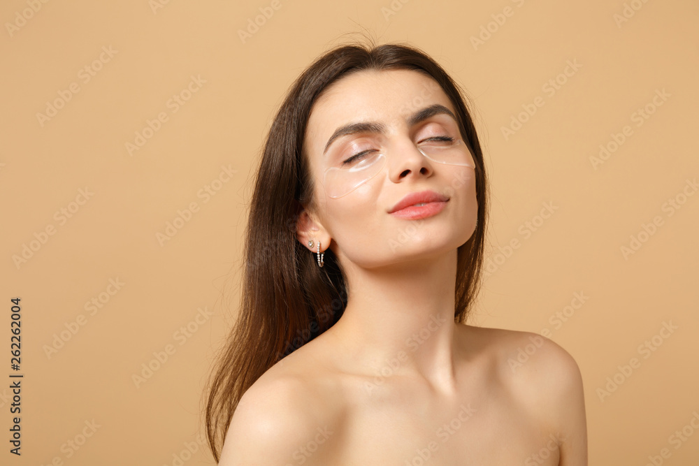 Fototapeta premium Close up half naked woman 20s with perfect skin, nude make up patches under eyes isolated on beige pastel wall background, studio portrait. Health care cosmetic procedures concept. Mock up copy space.