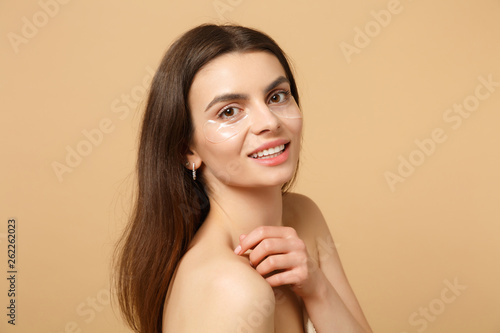 Close up half naked woman 20s with perfect skin, nude make up patches under eyes isolated on beige pastel wall background, studio portrait. Health care cosmetic procedures concept. Mock up copy space.