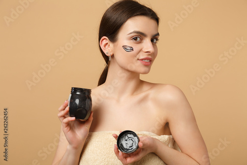Close up brunette half naked woman 20s with perfect skin, nude make up black mask isolated on beige pastel wall background, studio portrait. Healthcare cosmetic procedures concept. Mock up copy space.