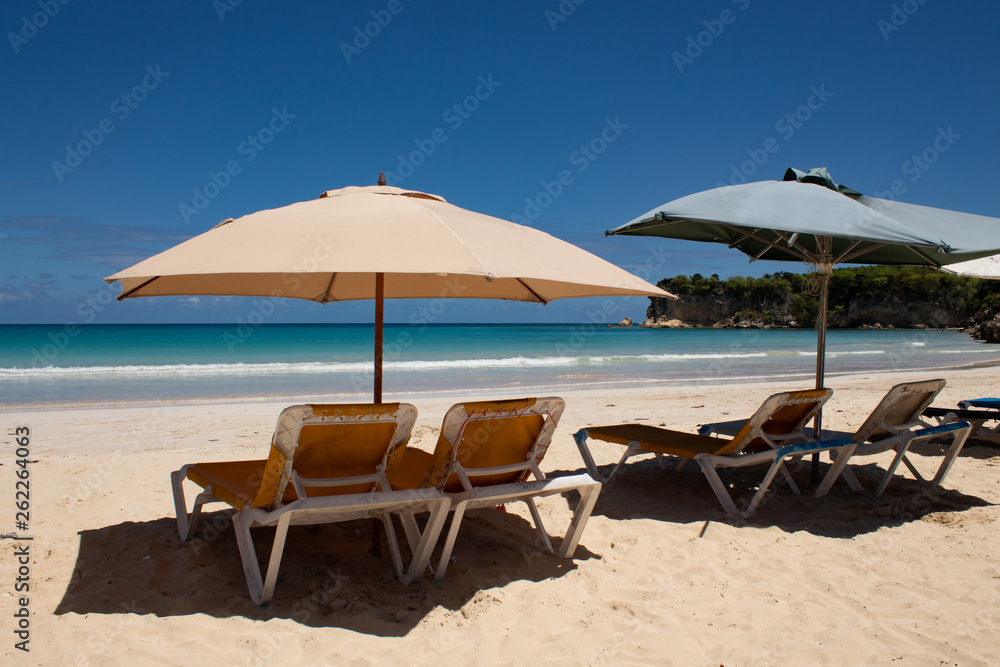 Caribbean colors: sunbeds and umbrellas on public beach, intense blue sea and sky: tropical paradise.