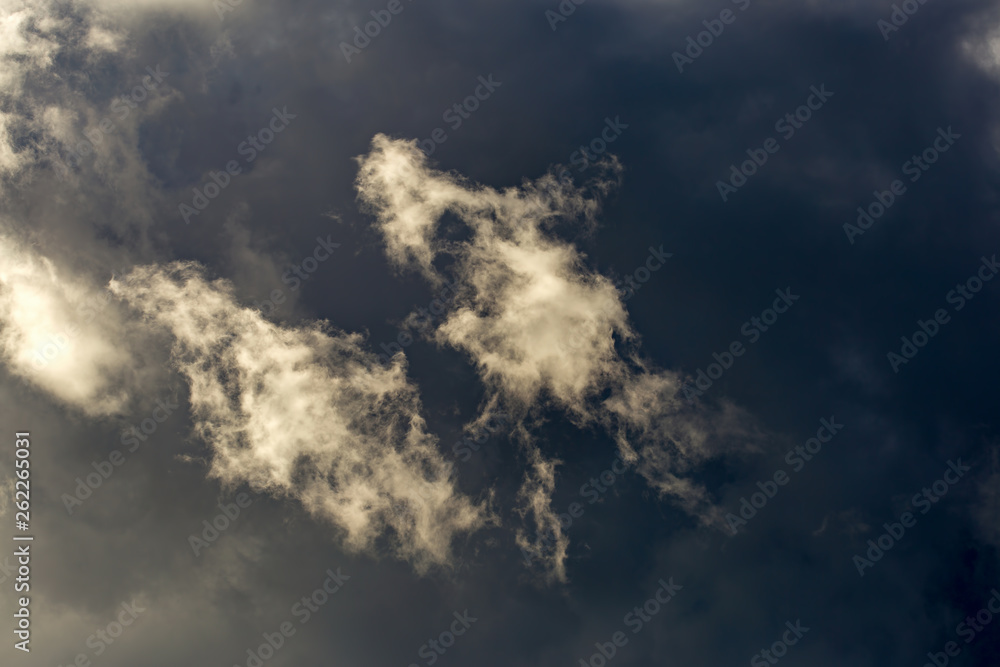 Two little soft clouds pass in front of a very gray cloud and recieve the sunbeams of the afternoon, over the Andean mountains of central Colombia. Two little soft clouds pass in front of a very gray cloud and recieve the sunbeams of the afternoon, over the Andean mountains of central Colombia.