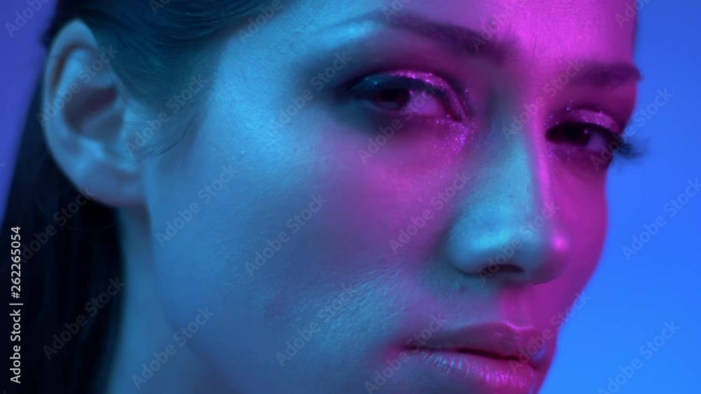 Fashion model in colorful neon lights watching with flirting eyes into camera and turns rightwards in studio. Fashion model in colorful neon lights watching with flirting eyes into camera and turns rightwards in studio.