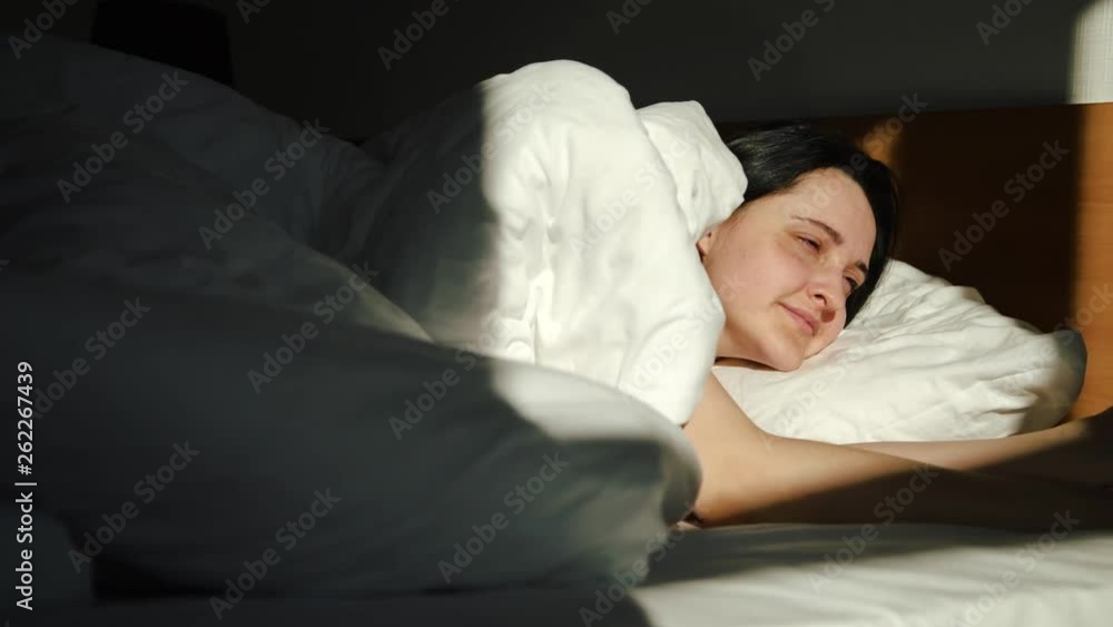 A young, sweet girl wakes up in bed in the morning and enjoys the first rays of the sun.Hugs the pillow A young, sweet girl wakes up in bed in the morning and enjoys the first rays of the sun.Hugs the pillow