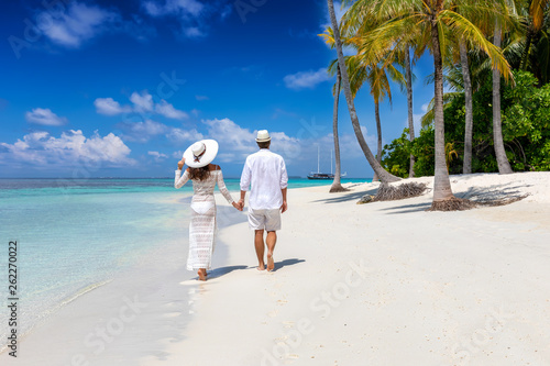 Elegant traveler couple walks down a tropical beach with coconut palm trees and turquoise waters in the Maldives islands photo