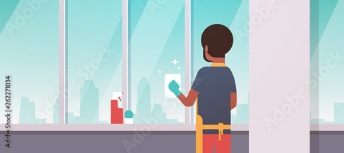 man in gloves and apron cleaning windows with rag cleaner spray rear view african american guy doing housework concept modern apartment living room interior flat portrait horizontal