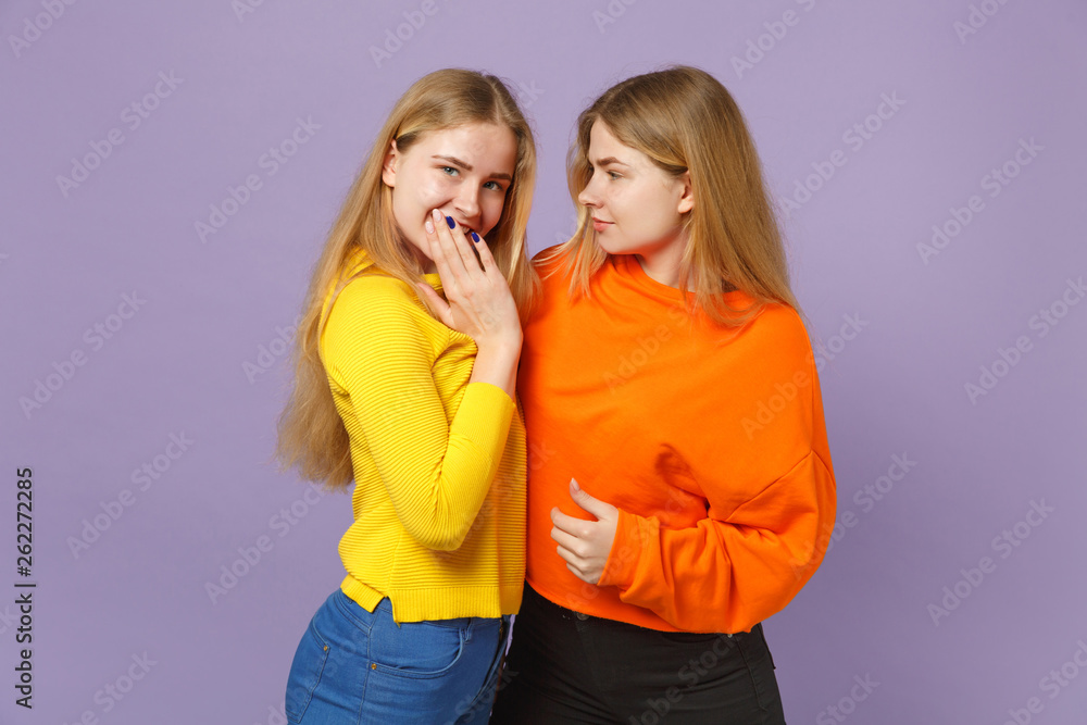 Two young blonde twins sisters girls in colorful clothes looking Two young blonde twins sisters girls in colorful clothes looking