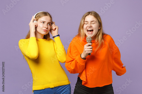 Two young blonde twins sisters girls in colorful clothes listen
