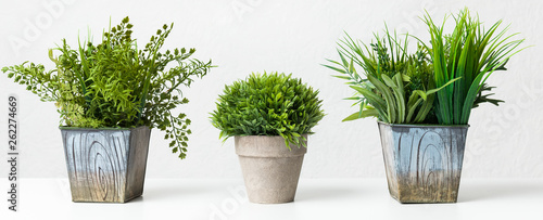 Variety of artificial houseplants against grey wall, crop