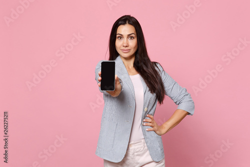 Portrait of beautiful young woman in striped jacket holding mobile phone with blank empty screen isolated on pink pastel wall background. People sincere emotions lifestyle concept. Mock up copy space.