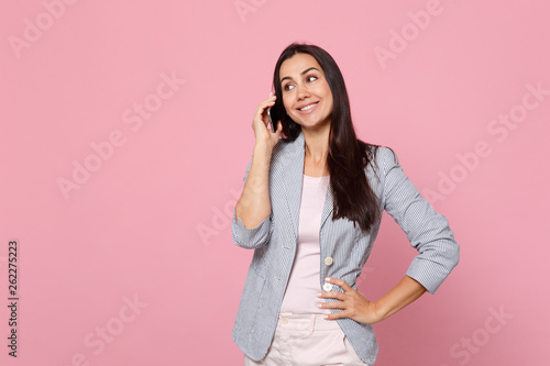 Smiling young woman in striped jacket talking on mobile phone, conducting pleasant conversation isolated on pink pastel wall background. People sincere emotions, lifestyle concept. Mock up copy space.