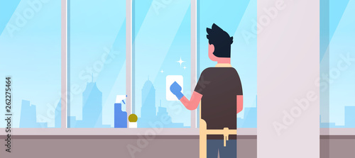 man in gloves and apron cleaning windows with rag cleaner spray rear view guy doing housework concept modern apartment living room interior flat portrait horizontal