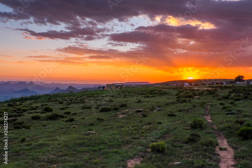 Sunset landscape over small village with mountains  clouds  orange sky and sun beams  Lesotho  Africa