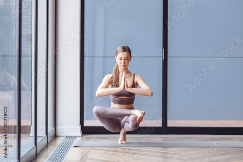 Young woman yoga instructor doing samatvamasana standing on a rug by the windows on the veranda of a country house. The concept of harmony of the body and peace