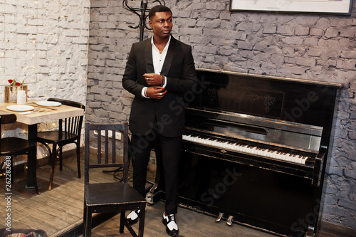 Canvas Print Strong powerful african american man in black suit standing against piano
