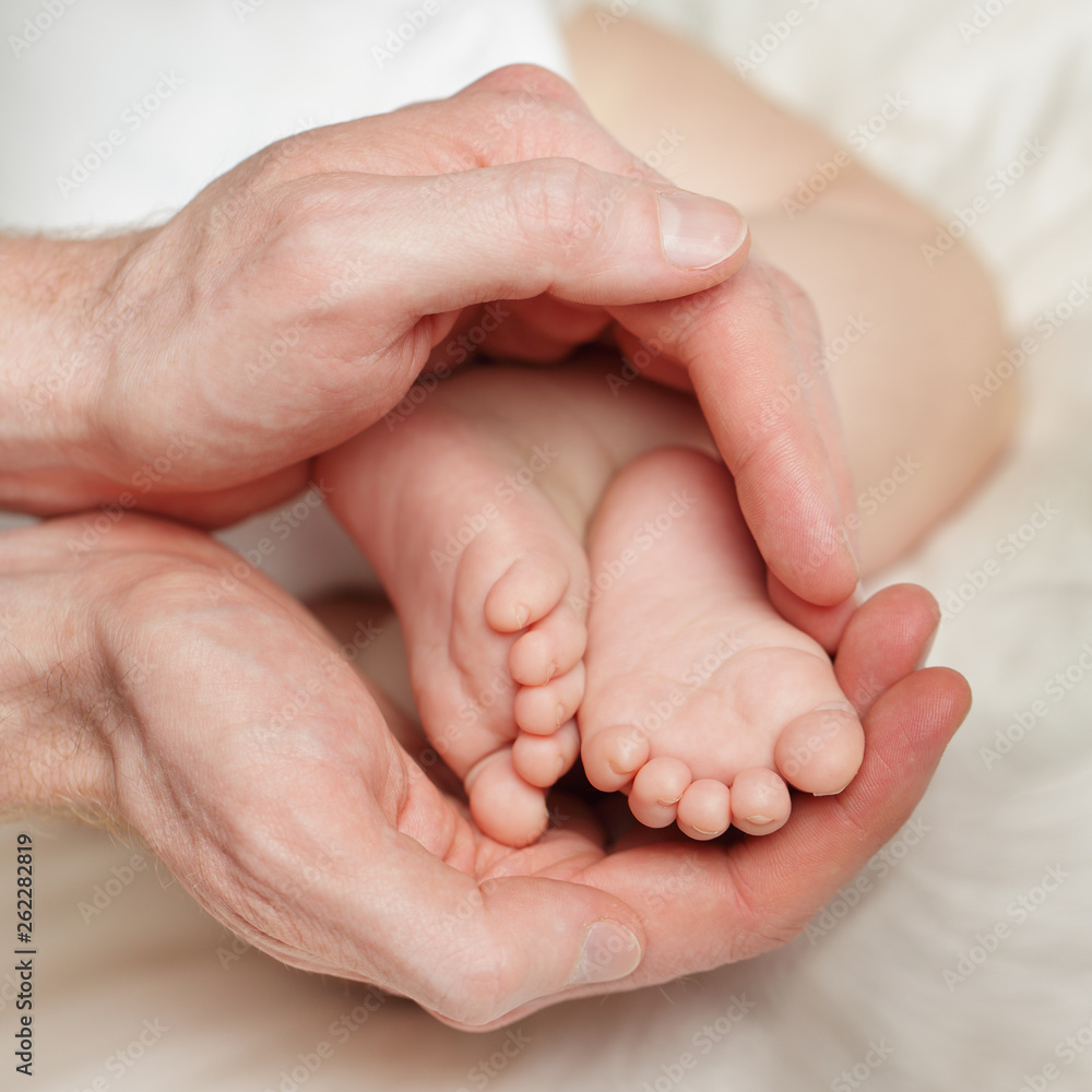 Male hands holding little feet of newborn baby